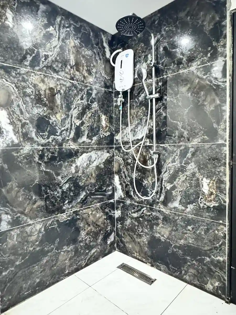 Modern corner shower featuring dark marble-style tiles and a water heater inside the Deluxe Suite at Turtle Seaweed Resort.